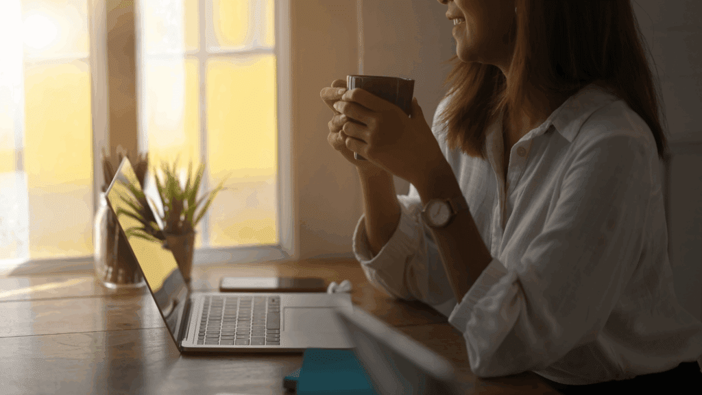 A dietitian sitting at their computer, holding a cup of coffee, with a leafy green plant in the background and natural light filling the space.