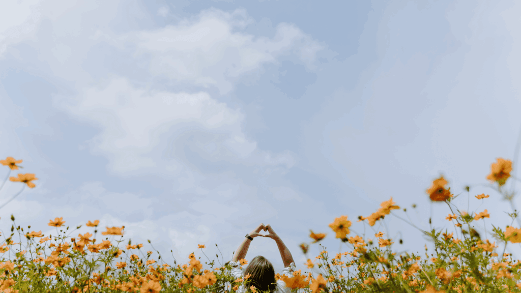 Woman in field of flowers, holding hands up in a heart shape to show her gratitude after working with a nutritionist for menopause.